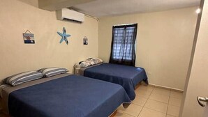 A room with two beds, a window with curtains, an air conditioner, and a door.