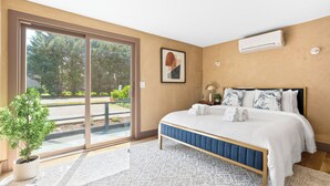Un dormitorio con un amplio ventanal corredera que da a un balcón, una cama con cabecera azul y una planta en maceta.