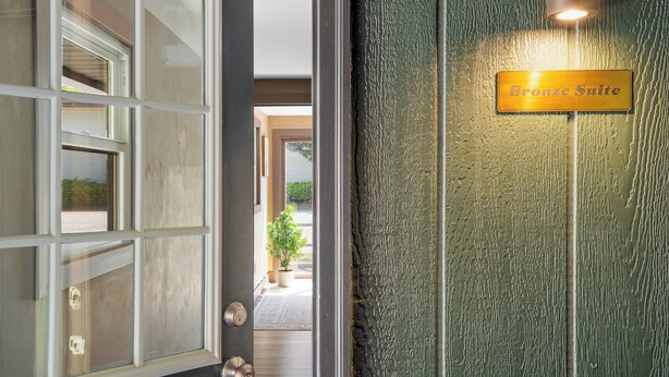Entrada de hotel con un cartel que dice "Bronze Suite", puerta de cristal y pared con textura.