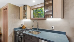 Una cocina con estufa a gas integrada, pileta de acero inoxidable y alacenas de madera.