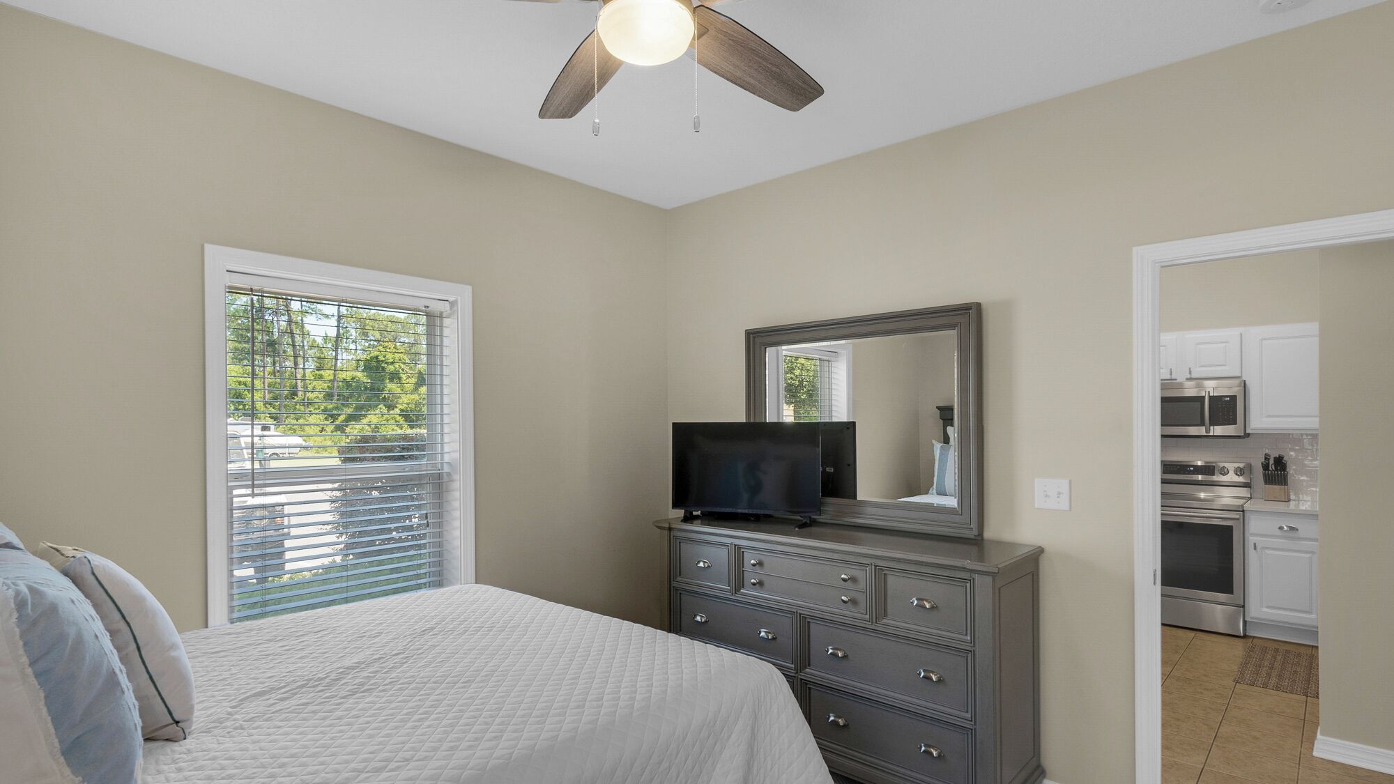 A bedroom with a bed, dresser, TV, and a ceiling fan.