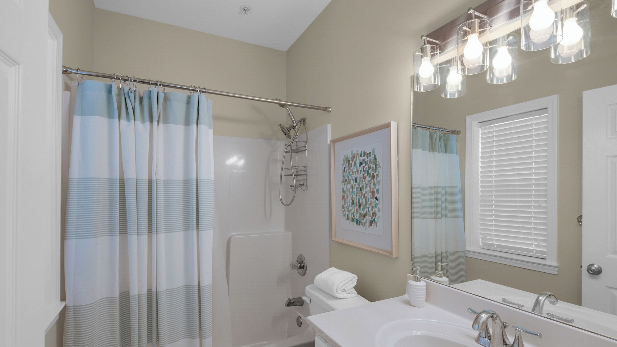 A bathroom with a shower, toilet, sink, and a framed artwork on the wall.