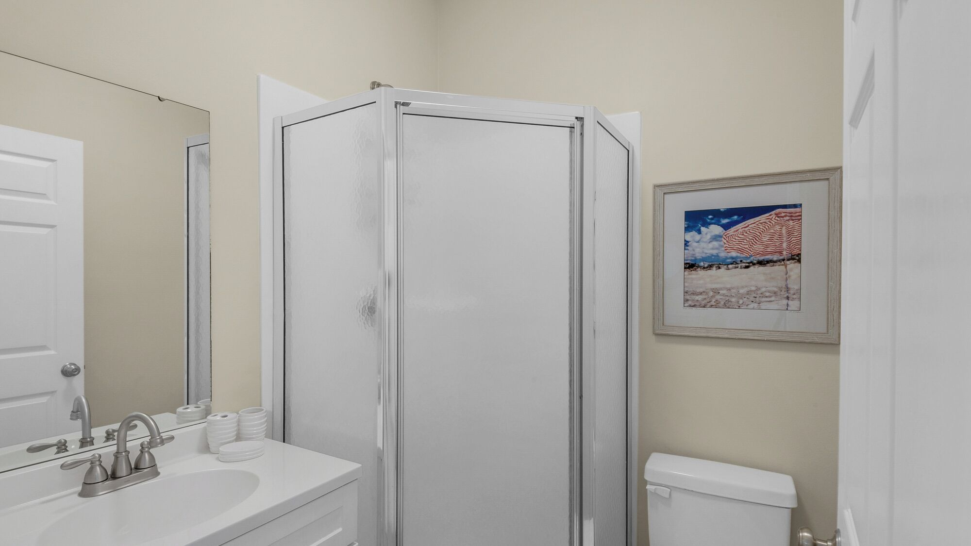 Ein Badezimmer mit Duschkabine, Waschbecken mit Armaturen, Toilette und einem gerahmten Bild an der Wand.