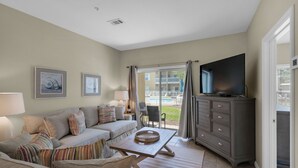 Un salon avec un canapé, une table basse, un téléviseur et une vue sur une piscine à l’extérieur.