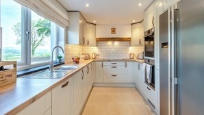 Une cuisine moderne avec des meubles blancs, un réfrigérateur en acier inoxydable et une fenêtre donnant sur un paysage pittoresque.