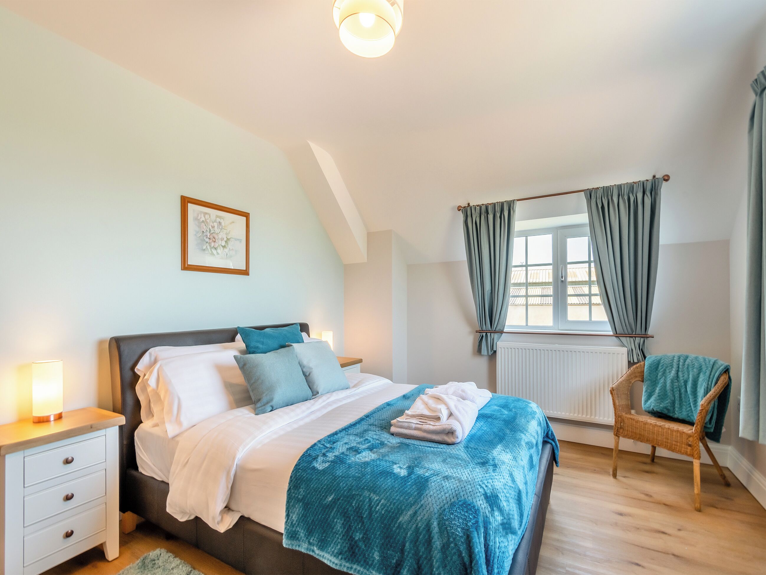 A bedroom with a bed, bedside table, chair, and a window with curtains.
