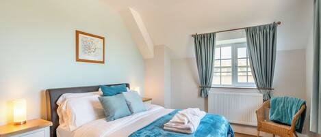 A bedroom with a bed, bedside table, chair, and a window with curtains.
