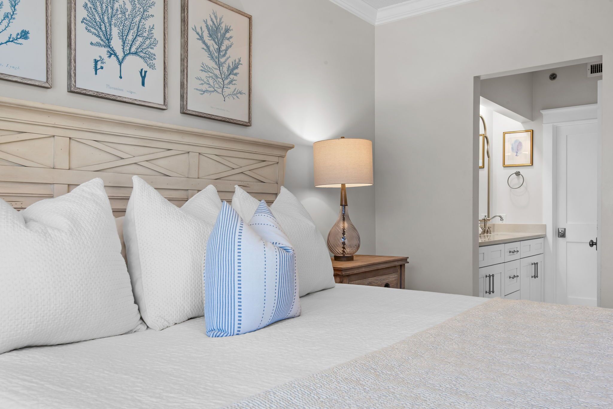 Un letto rifatto con cuscini a righe bianche e blu, una testiera in legno e una lampada da comodino.