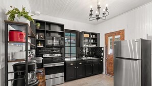 A modern kitchen with black cabinetry, stainless steel appliances, and a wooden door. - Walk to the Beach, Historic Cottage  (Galveston)