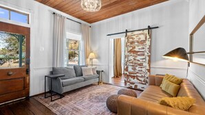 A living room with a grey sofa, a brown leather sofa, a chandelier, and a rustic wall. - Walk to the Beach, Historic Cottage  (Galveston)
