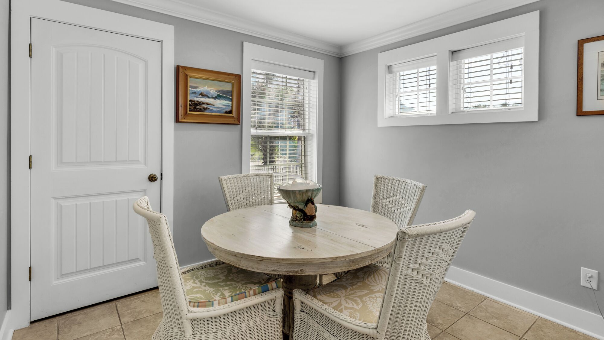 A dining area with a round table, four wicker chairs, and a vase centerpiece.