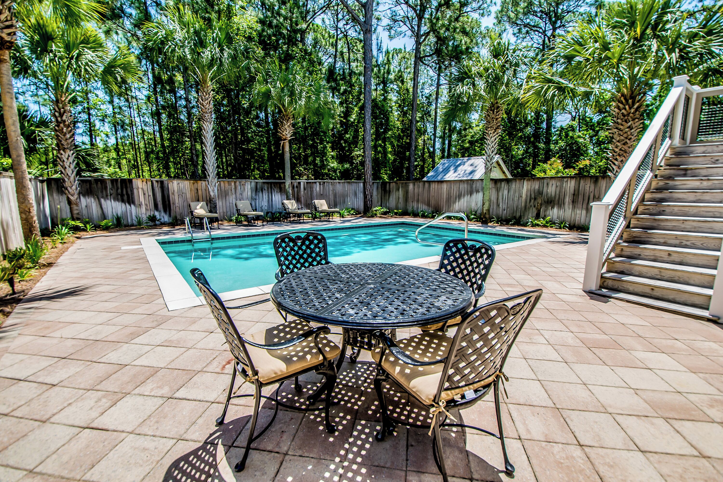 A backyard with a swimming pool, a wooden deck, and a table with chairs.