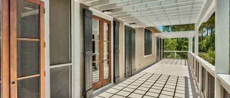 A covered outdoor area with a grid floor, sliding glass doors, and a pergola structure.