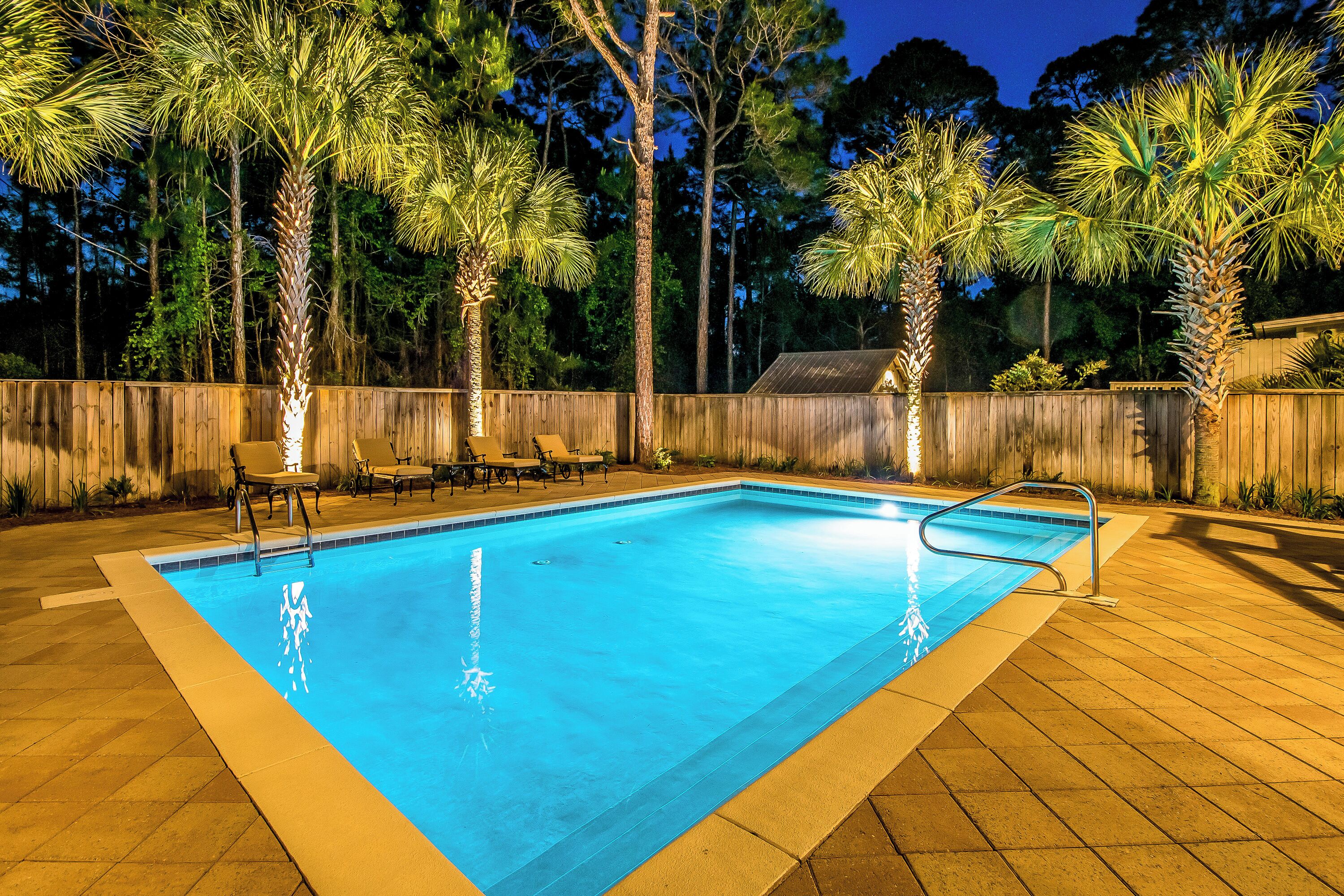 A rectangular swimming pool with a wooden deck surrounding it, equipped with a metal ladder and a few lounge chairs.