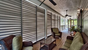 Varanda coberta com móveis de vime, ventiladores de teto e janelas amplas com persianas.