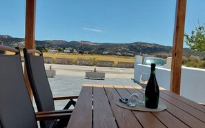 A wooden table with a bottle and glasses, overlooking a scenic landscape with hills and a clear sky. - Marven´s Apartment (Zefiria)