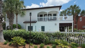 A two-story white building with a balcony, surrounded by palm trees and a white fence. - Large Private Pool ~ Minutes to Beach ~ Gulf Side ~ Seagrove (Santa Rosa Beach)