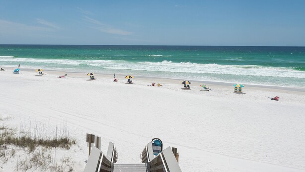 Une plage de sable blanc, avec des vagues et des parasols.