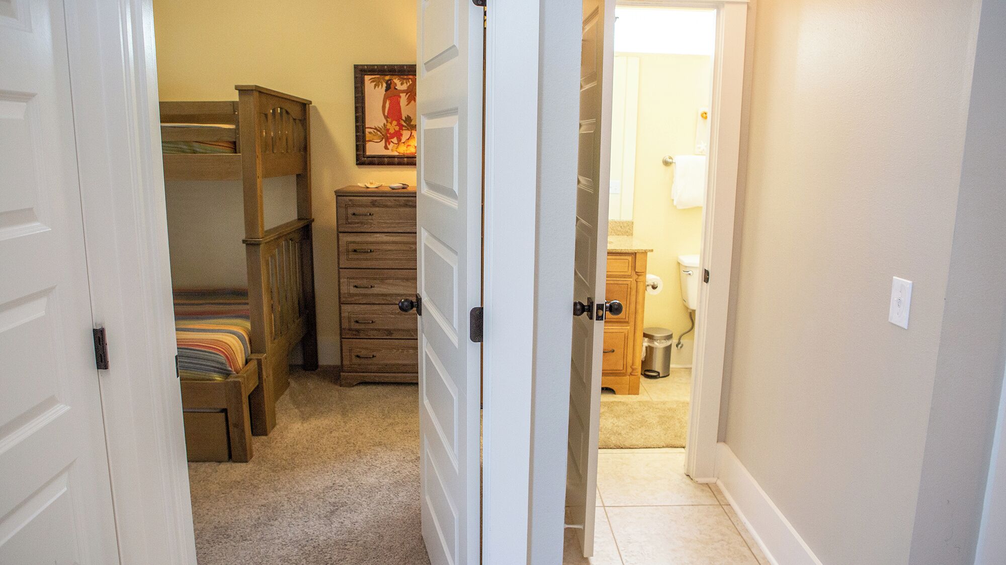 A bedroom with a bunk bed, a dresser, and a painting on the wall.