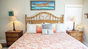 A bedroom with a wooden headboard, floral bedspread, and multiple pillows with tropical designs. There are two bedside tables with lamps and a painting of a beach scene on the wall. - Large Private Pool ~ Minutes to Beach ~ Gulf Side ~ Seagrove (Santa Rosa Beach)