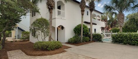 A two-story white building with a balcony, surrounded by palm trees and a brick pathway.