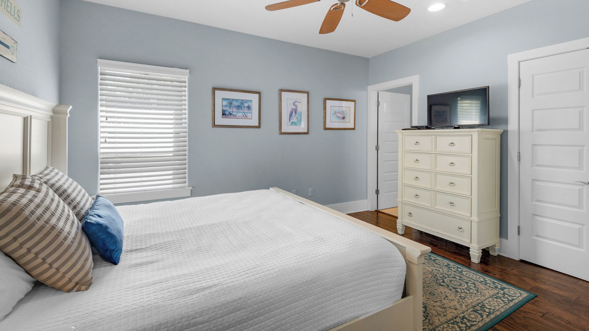 A bedroom with a bed, a dresser, a television, and framed pictures on the wall.
