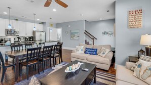 A modern living room with a dining area, kitchen, and a staircase leading to another level. - Blue Mountain Beach - Sleeps 12 - Steps From Pool (Santa Rosa Beach)