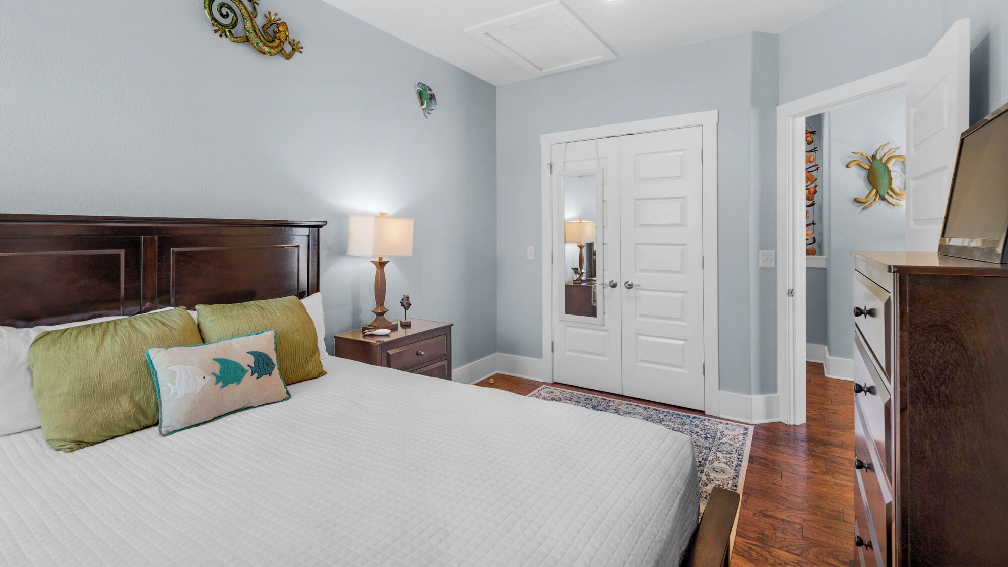 Une chambre à coucher avec un grand lit, une table de chevet avec une lampe, une commode et une porte dotée d’un miroir.