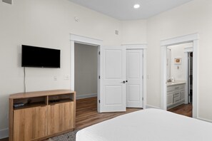 A bedroom with a bed, a TV mounted on the wall, a wooden cabinet, and white doors leading to other rooms. - Luxury 4-bedroom Vacation Home With Unparalleled Gulf Views (Santa Rosa Beach)