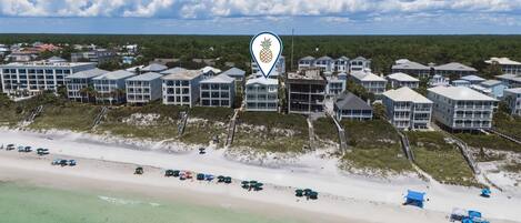 A coastal hotel with multiple buildings, a beach, and a clear sky.