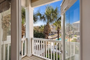 A balcony with a view of a pool, palm trees, and a building in the background. - Luxury 4-bedroom Vacation Home With Unparalleled Gulf Views (Santa Rosa Beach)
