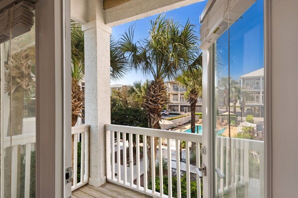 A balcony with a view of a pool, palm trees, and a building in the background.
