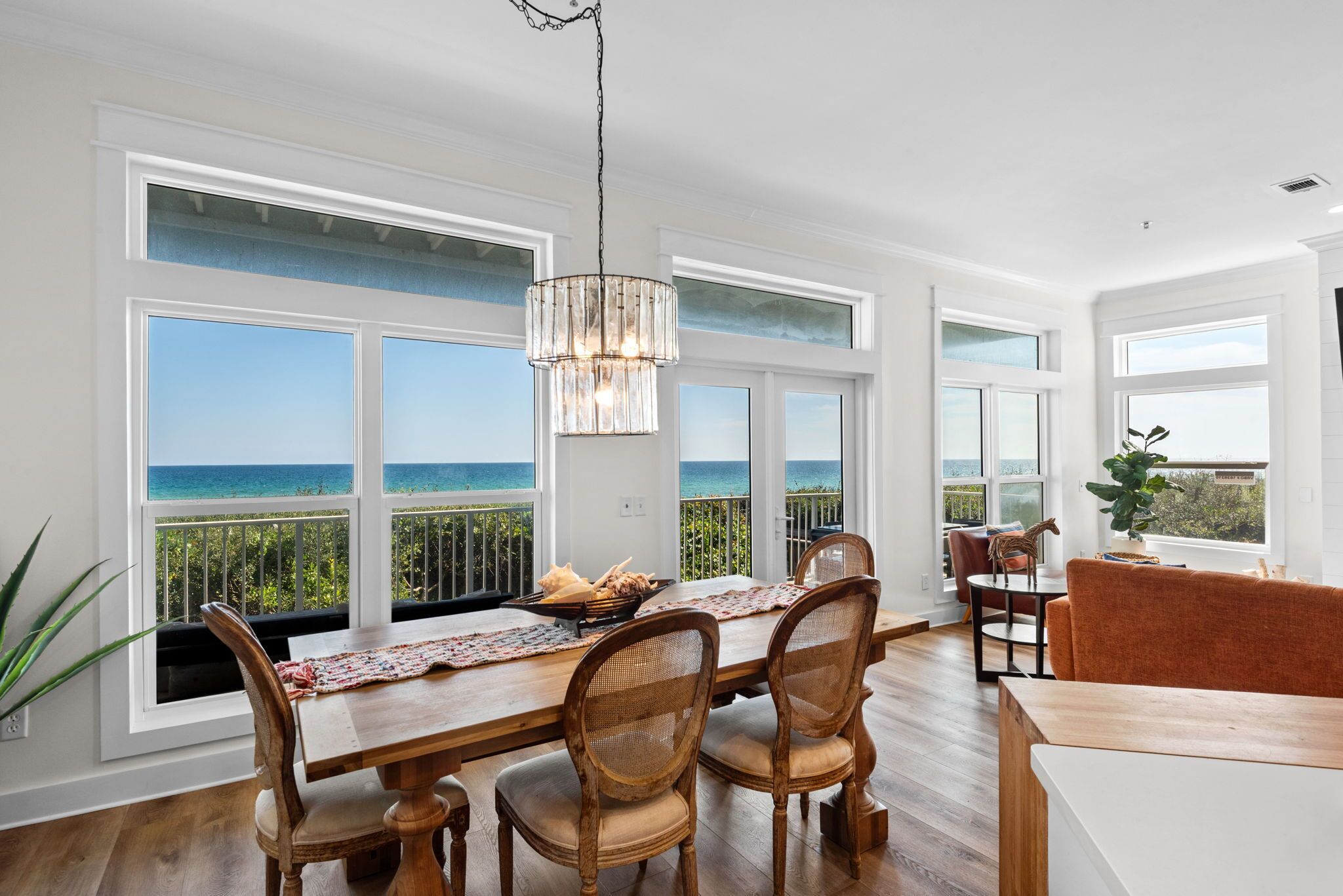 A dining area with a view of the ocean, a chandelier, and a wooden table with chairs.