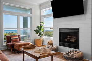 A living room with a fireplace, large windows, a sofa, and a television. - Luxury 4-bedroom Vacation Home With Unparalleled Gulf Views (Santa Rosa Beach)