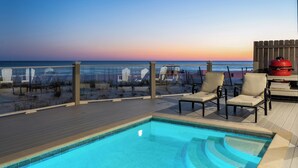Un espace piscine offrant une vue sur la plage et l’océan au coucher du soleil.