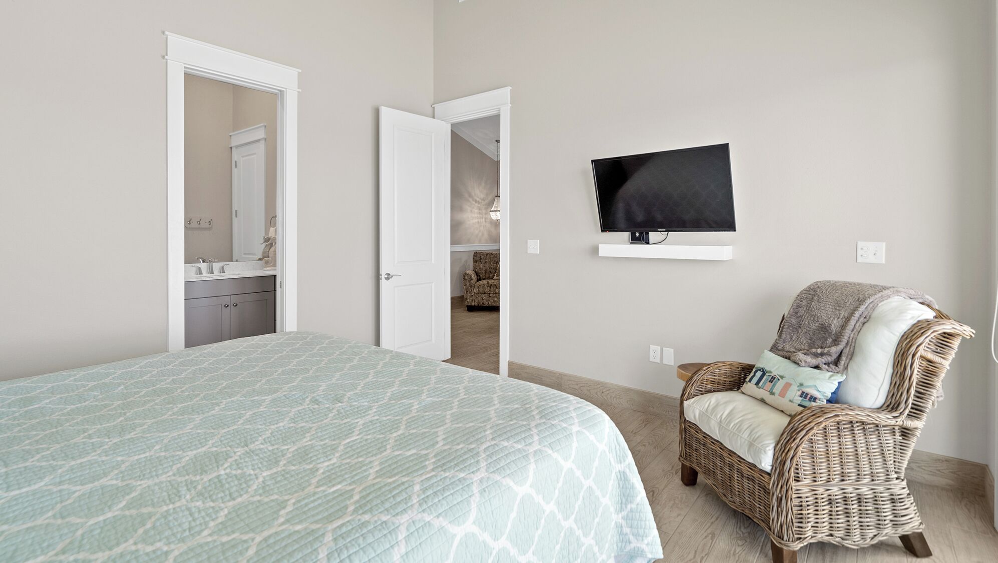 Een slaapkamer met een bed, een rieten stoel, een televisie en een badkamer, zichtbaar door een geopende deur.
