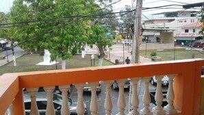 A balcony with a view of a street, including cars and a building with a sign that reads "SALLE DE CONFERENCIA". - Apartment with King bed in the center, sugar city! (Orange Walk)