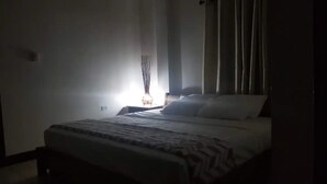 A dimly lit hotel room with a bed, a nightstand, and a lamp. - Apartment with King bed in the center, sugar city! (Orange Walk)