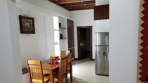 A dining area with a wooden table and chairs, a refrigerator, and a door leading to another room. - Apartment with King bed in the center, sugar city! (Orange Walk)