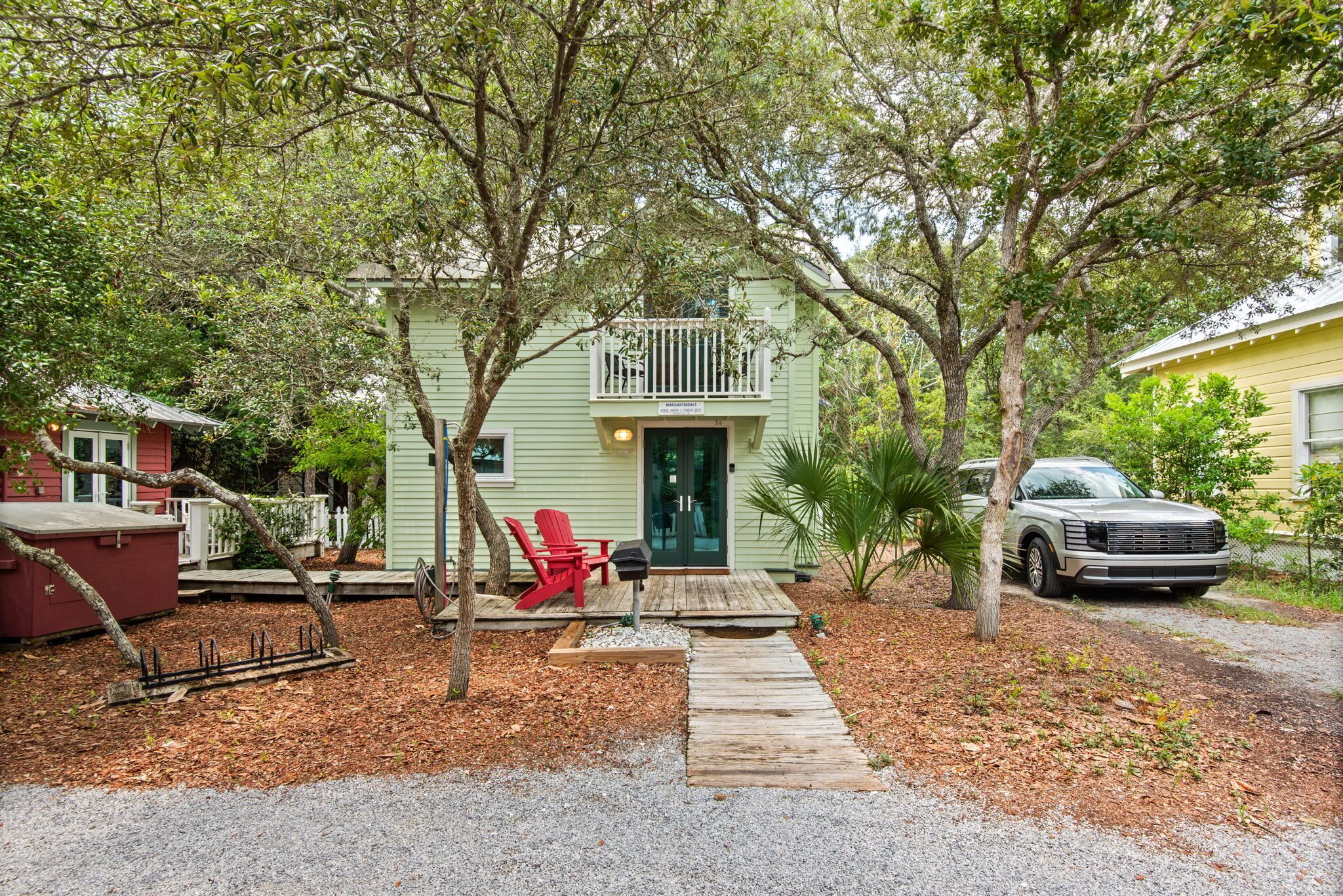 A green house with a porch, a red chair, and a mailbox.