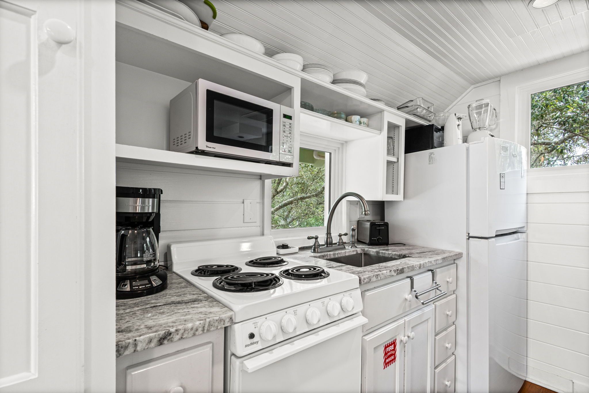 A kitchen with white cabinetry, a stove, a microwave, a coffee maker, and a refrigerator.
