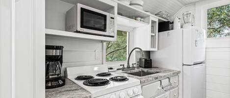 A kitchen with white cabinetry, a stove, a microwave, a coffee maker, and a refrigerator.