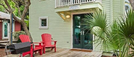 Una casa verde clara con balcón, buzón y dos sillas Adirondack rojas en el porche.