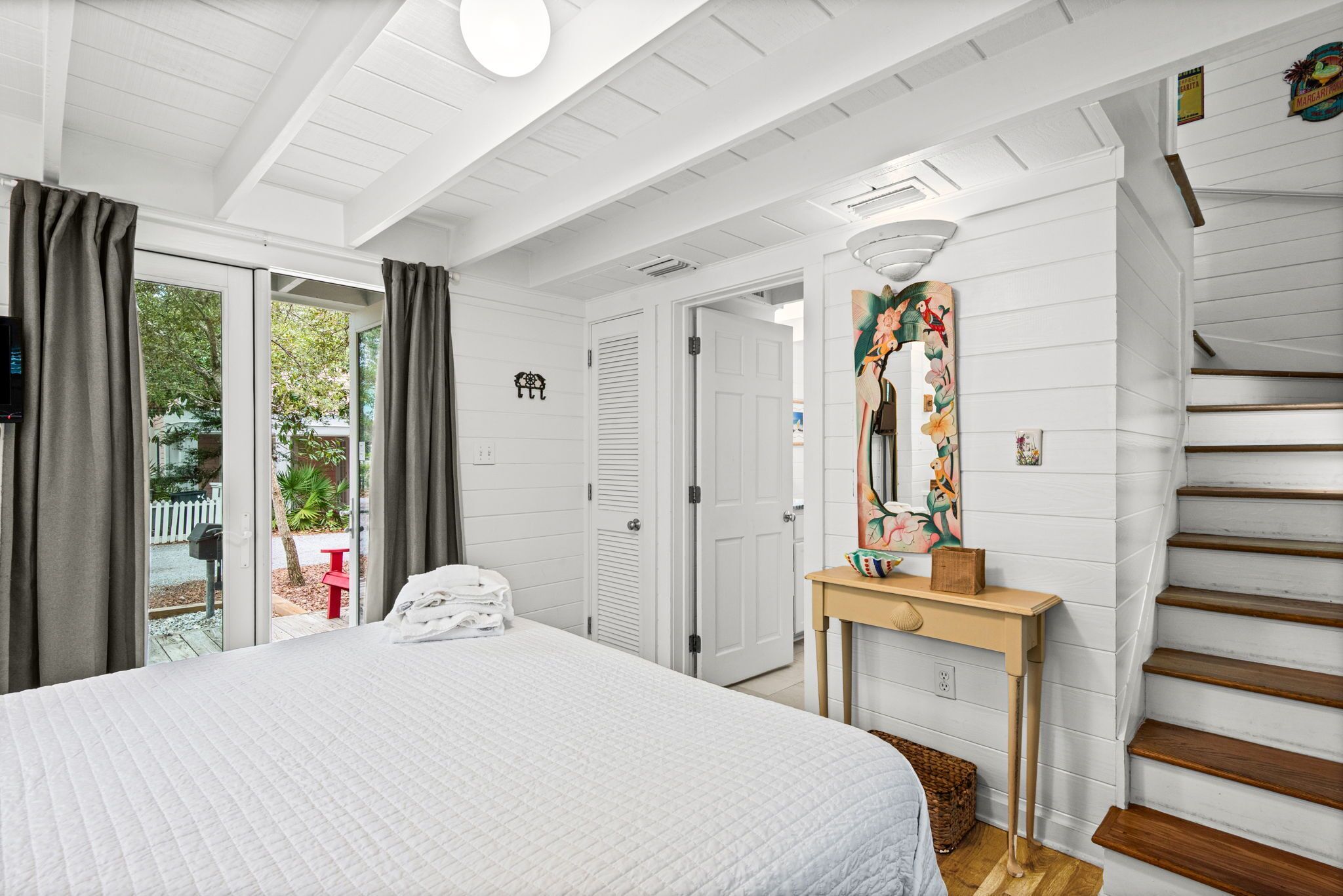 A bedroom with a bed, a wooden console table, a mirror, and a staircase.