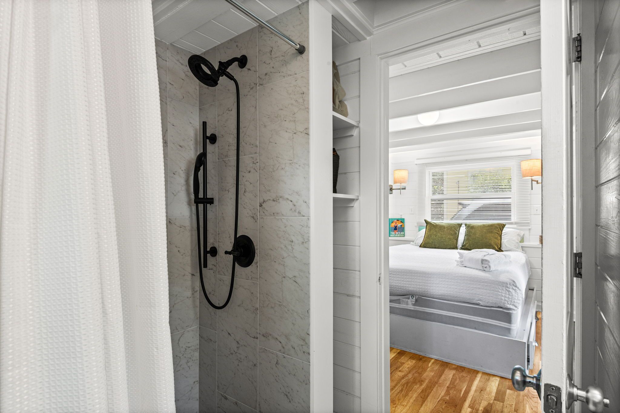 A bathroom with a shower, a bed with a view, and a wooden floor.