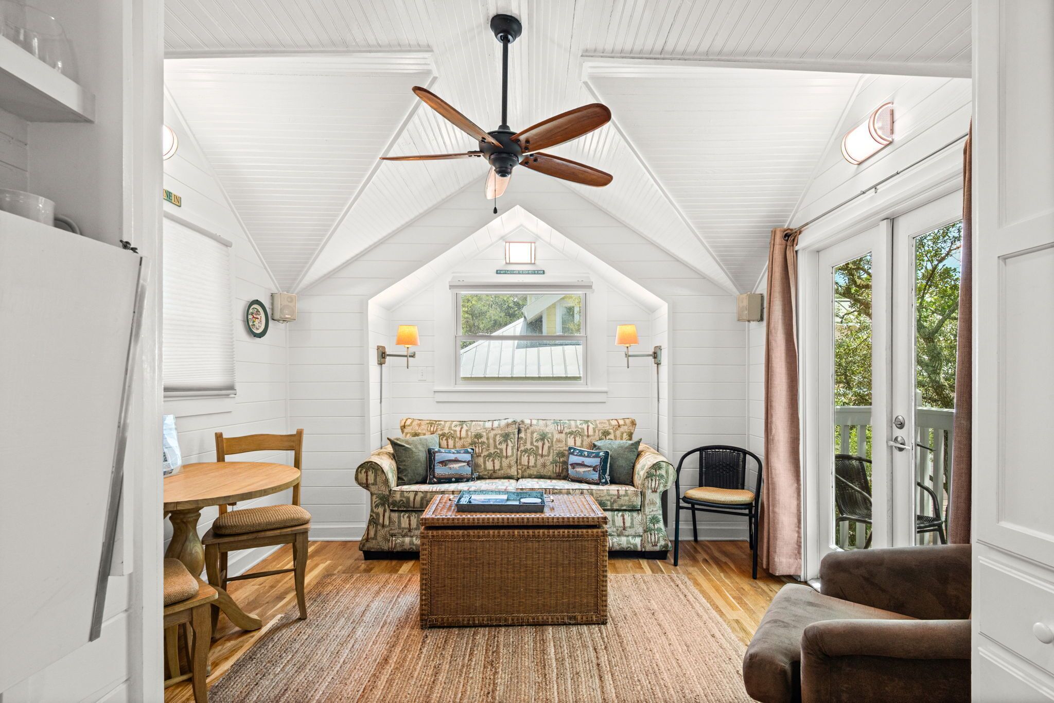 A cozy room with a ceiling fan, a sofa with patterned cushions, a wicker coffee table, and a dining area with a table and chairs.