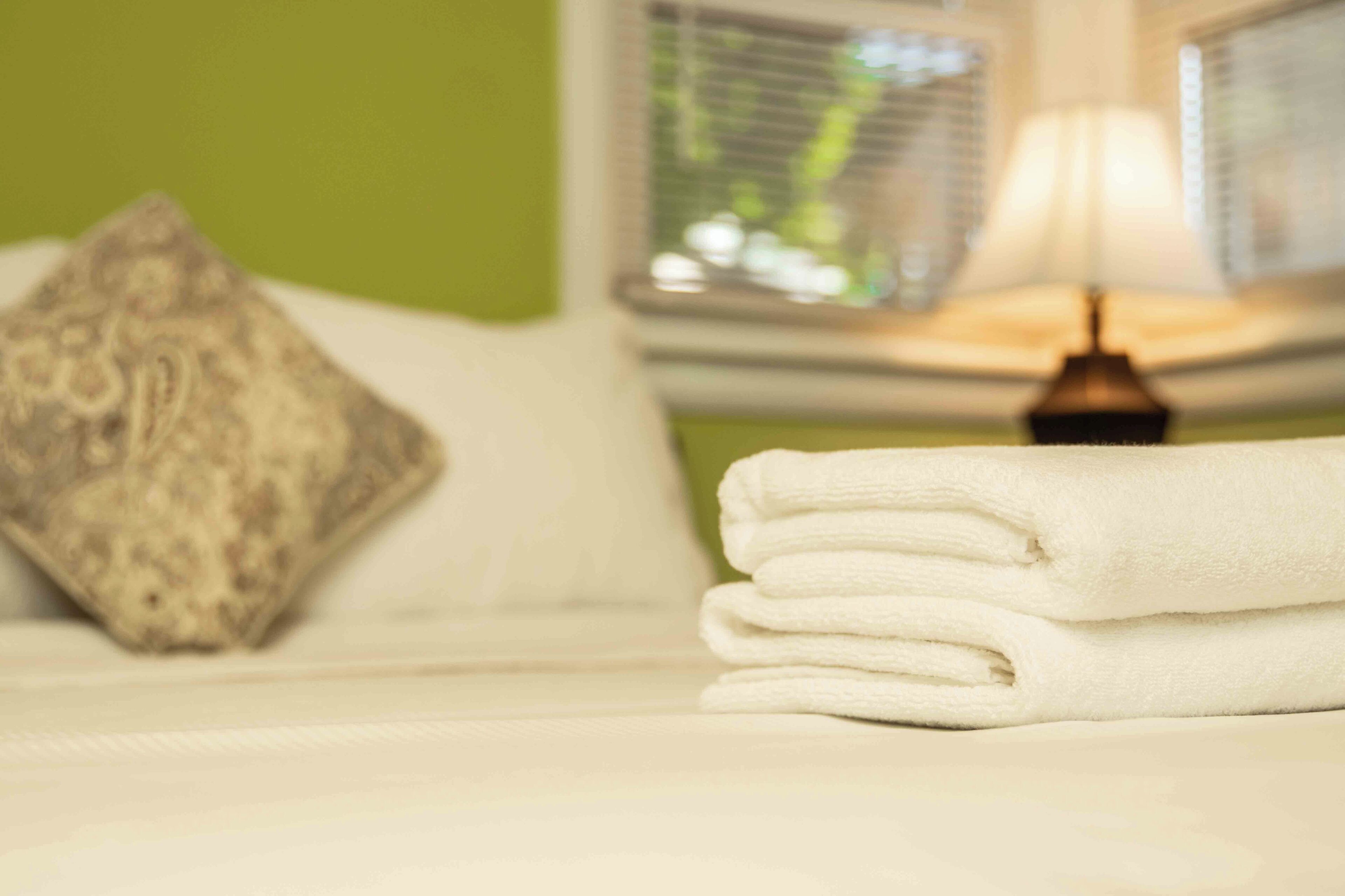 A neatly made bed with a pillow and a stack of folded towels.