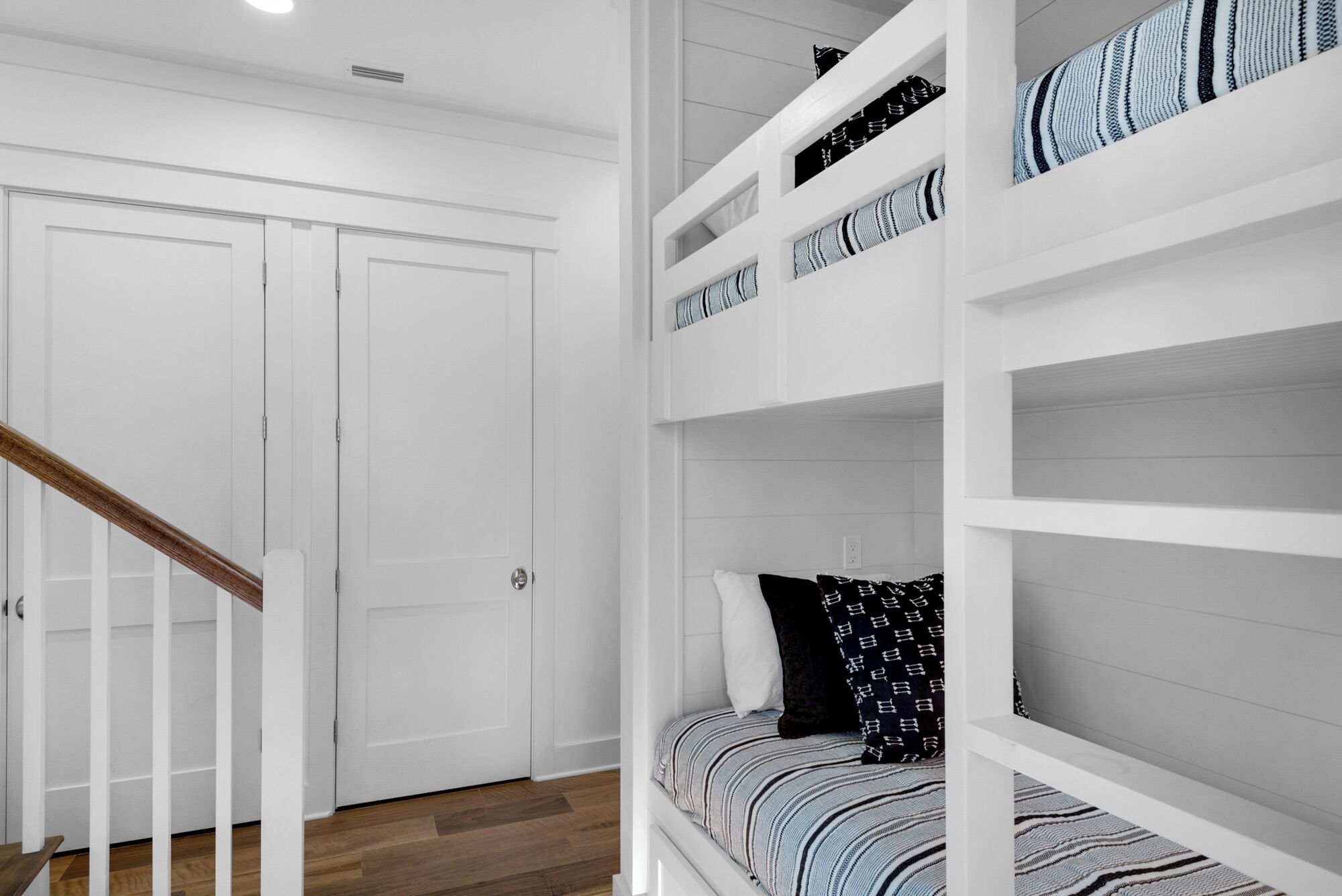 A bedroom with a bunk bed, a wooden staircase, and white walls.
