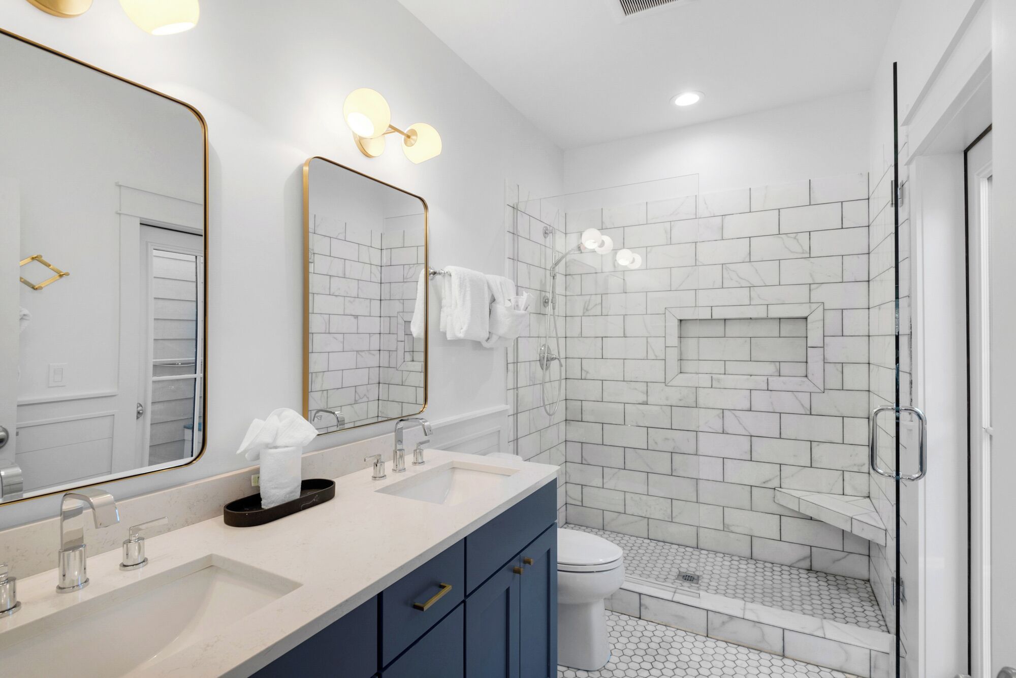 A modern bathroom with a double sink, a glass shower enclosure, and a large mirror with wall sconces.