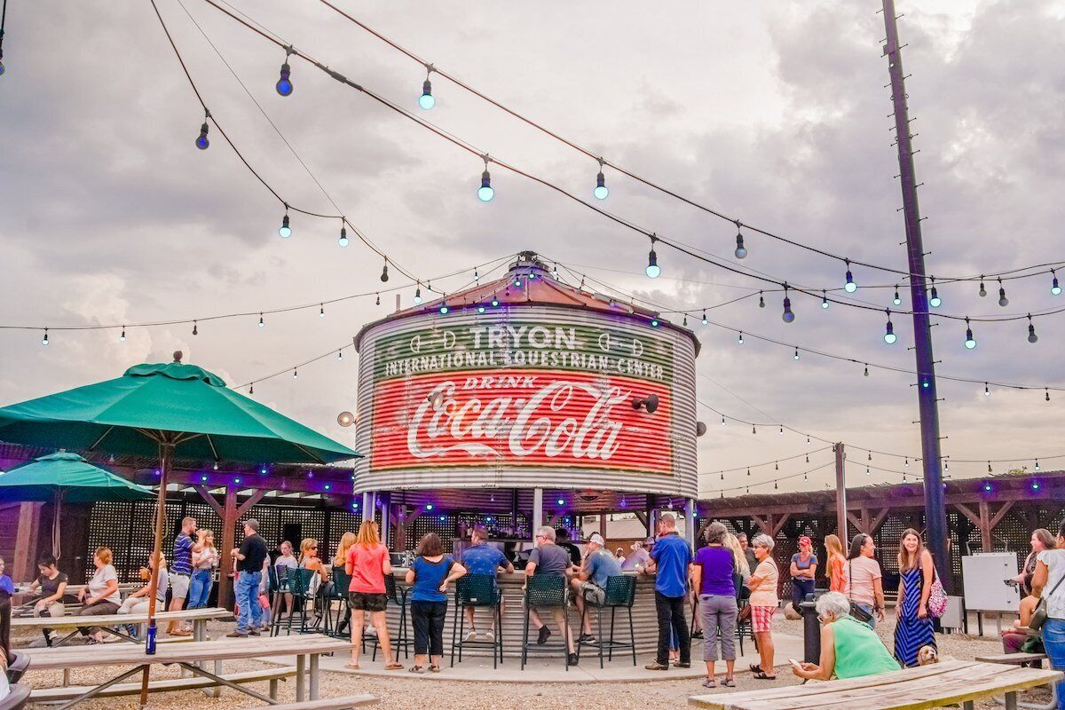 An outdoor seating area with tables and umbrellas, a Coca-Cola branded structure, and string lights.